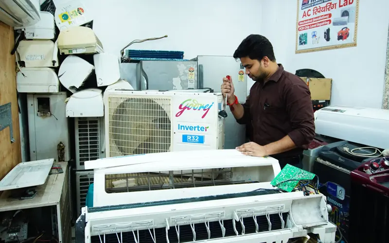 Technician repairing an air conditioner unit in New Delhi workshop.