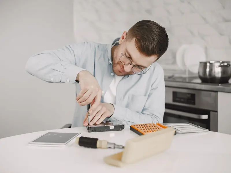 Man wearing glasses using a screwdriver to fix a device on a kitchen table.