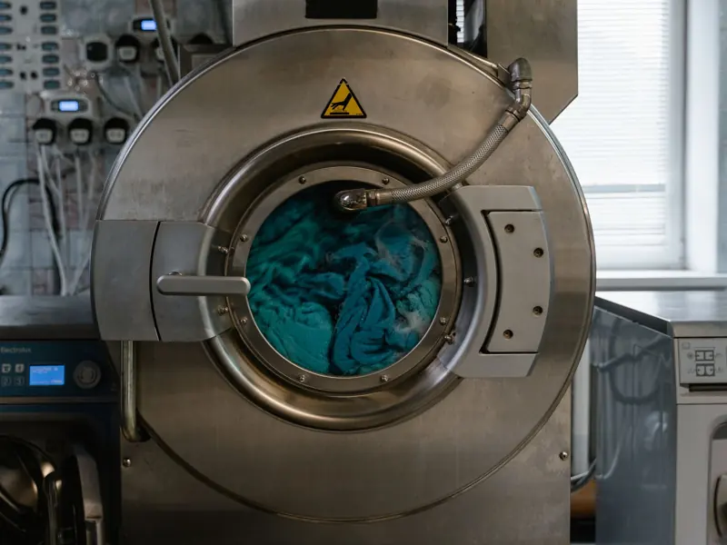 Large industrial washing machine with blue fabrics in a laundry facility.