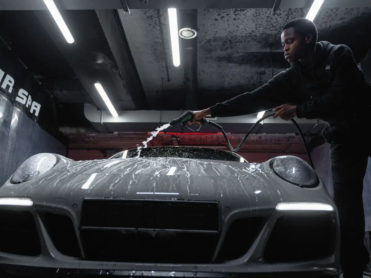 African American man cleaning a white sports car at an indoor car wash. Low angle perspective.