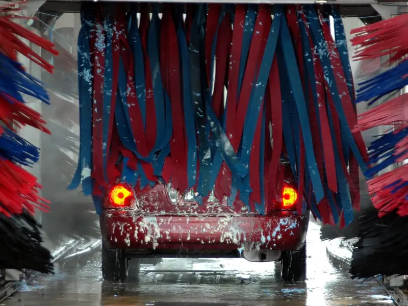 Red car being cleaned in an automated car wash with colorful brushes and soap suds.