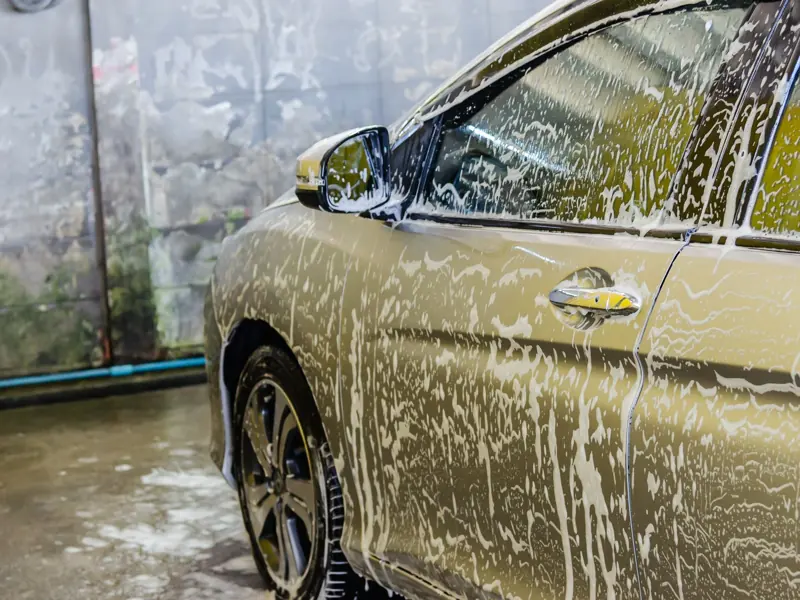 A car being washed with soap at a car wash service, highlighting cleaning and care.