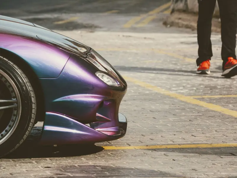 Close-up of a purple sports car next to a person in vivid sneakers on a cobblestone street.