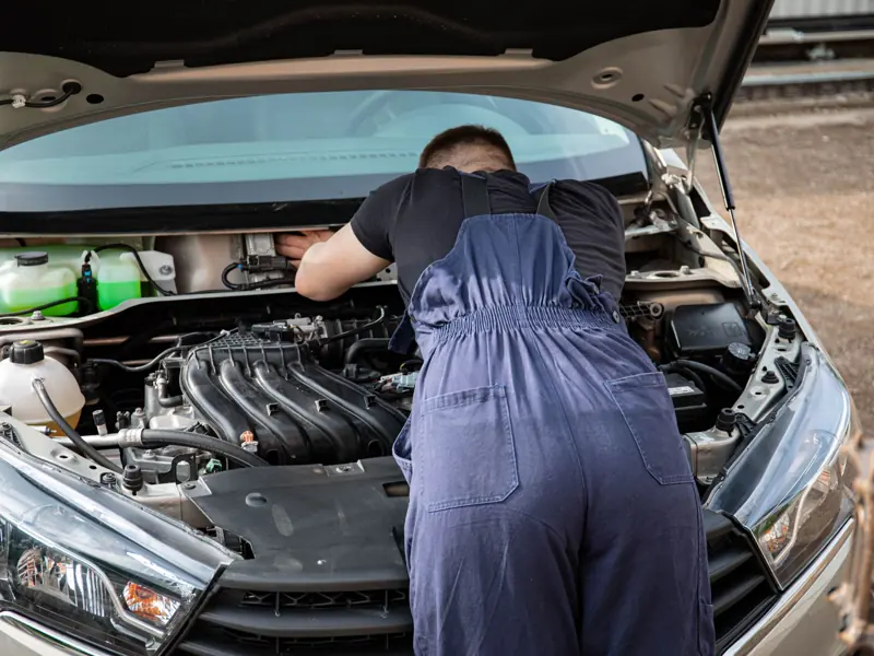An automotive mechanic performing engine maintenance on a car outdoors, showcasing mechanical skills.