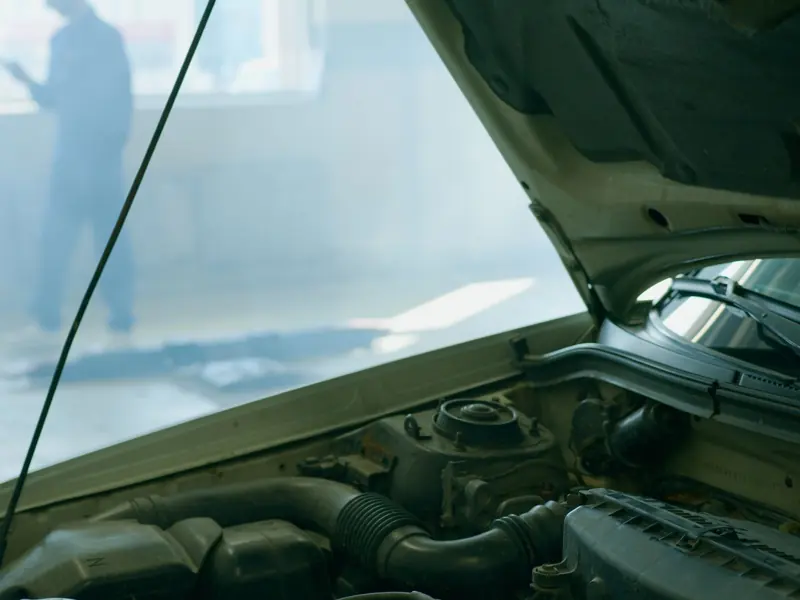 Detailed view of an open car hood in a mechanic workshop with a mechanic blurred in the background.