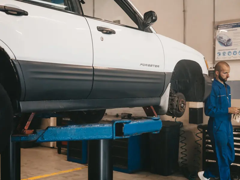 Mechanic evaluating a car on a lift for maintenance in an auto workshop.