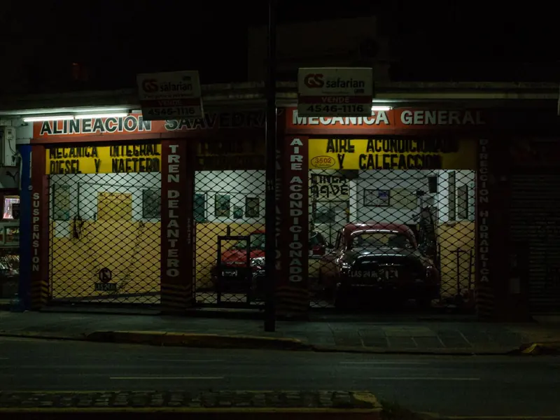 Dimly lit urban garage storefront at night featuring vintage cars.
