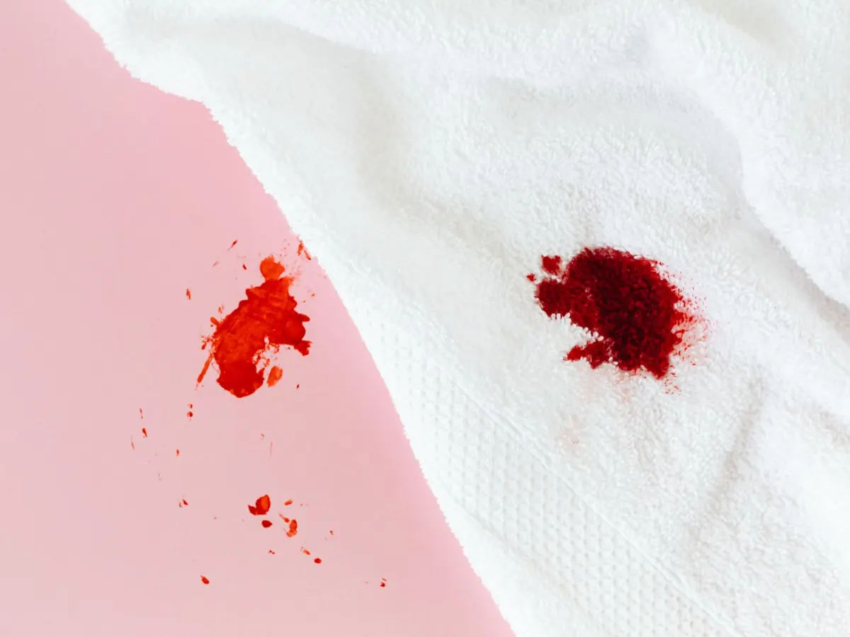 Red blood stain on a white towel spread over a pastel pink background, close-up shot.