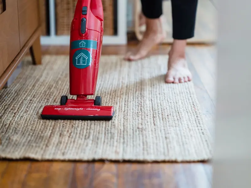 A red vacuum cleaner on a carpet in a stylish home setting with barefoot user.