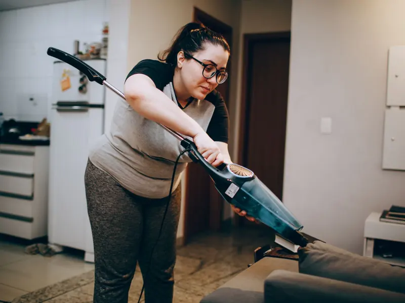 A woman vacuuming a couch in a cozy living room setting, emphasizing daily housework.