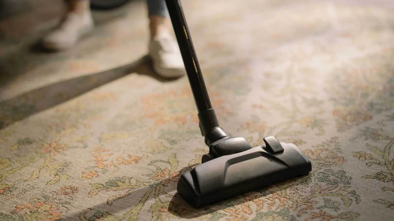 Close-up of a vacuum cleaner on a patterned carpet in a sunlit room, capturing a moment of household cleaning.