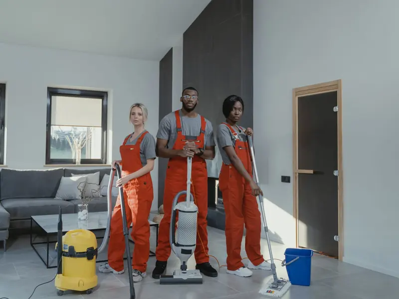 Diverse cleaning team in red uniforms ready to sanitize a modern living room with vacuum and mop.