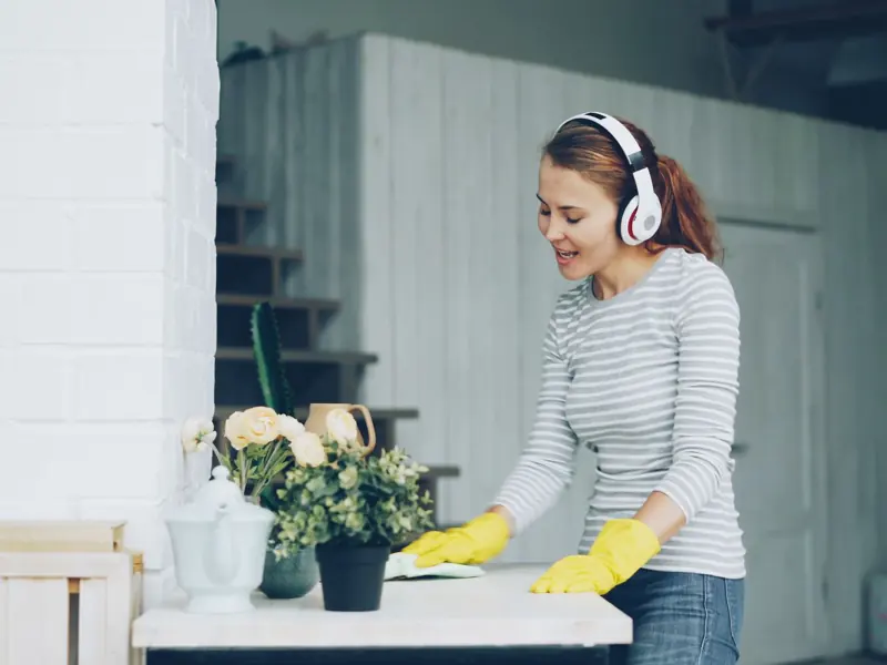 A woman with headphones cleaning indoors, surrounded by plants.