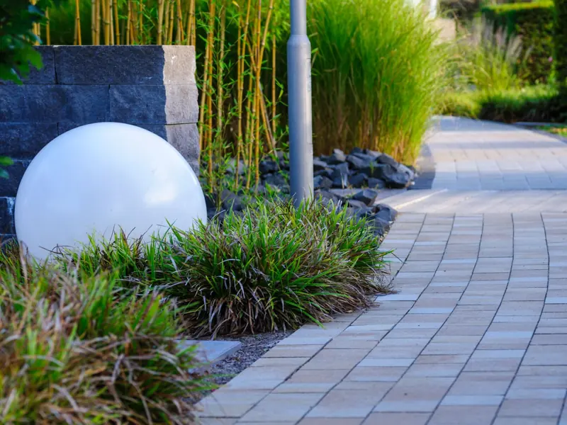 A tranquil garden pathway featuring a modern white sphere and lush greenery.