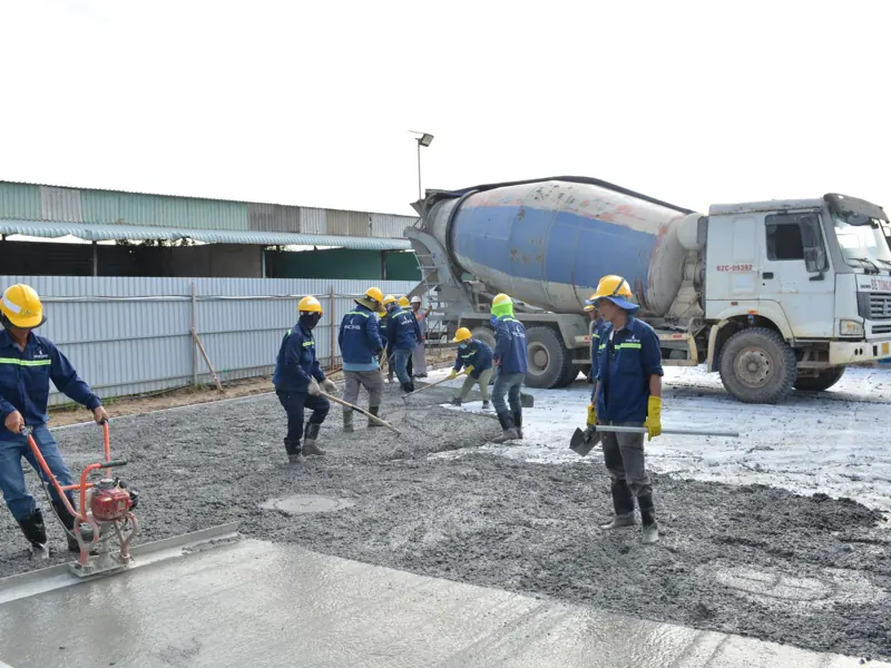 Workers in safety gear pouring concrete outdoors with a cement mixer truck.