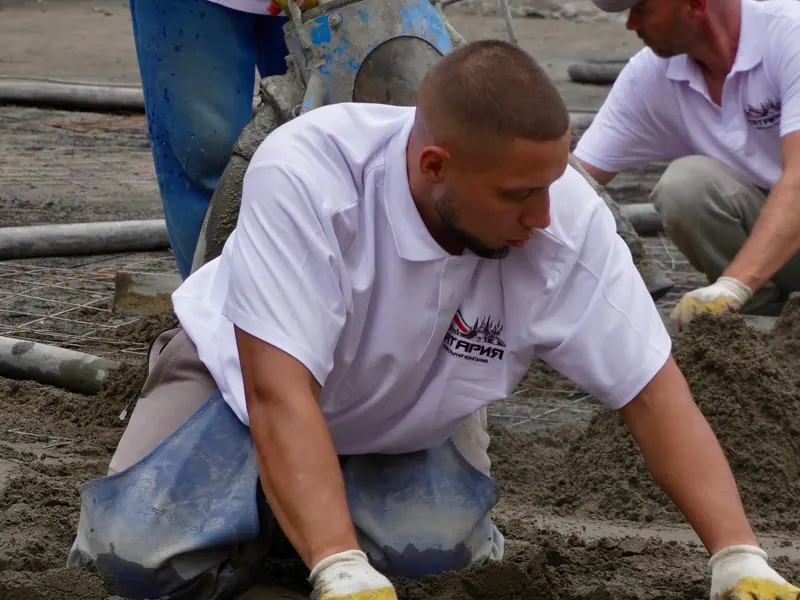 Construction workers expertly level wet concrete for a smooth finish on a building site.