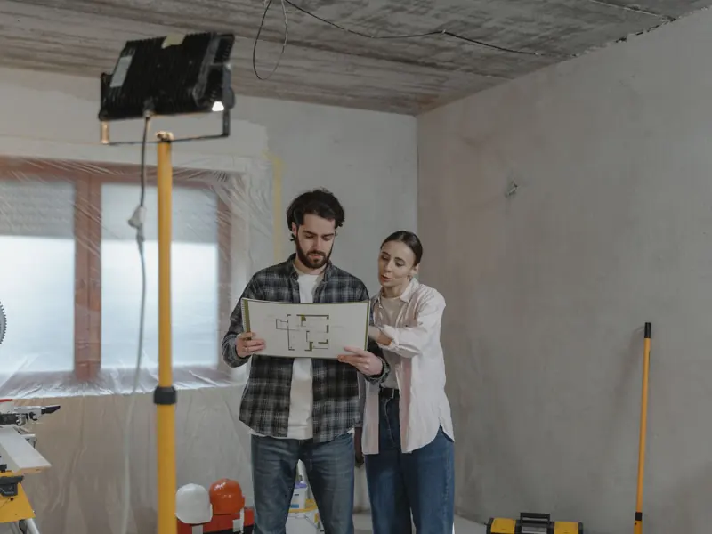 A couple examines blueprints in a partially renovated room, planning home improvements.