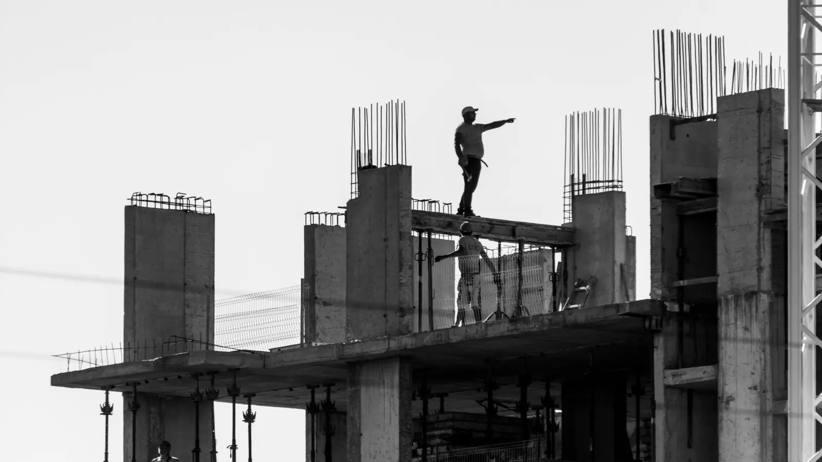 Silhouette of construction workers on a building site with one pointing towards the distance.