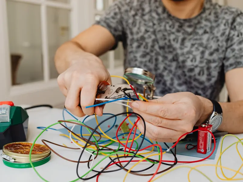 Person using pliers to cut through colorful electrical wires, showcasing DIY electronics work.
