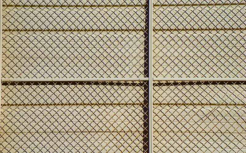 Detailed pattern of a chain-link fence casting shadows, creating a textured grid effect.