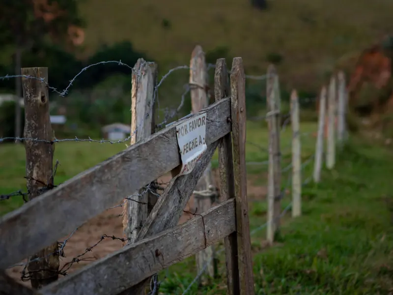 Close-up of a rustic wooden fence with a warning sign in a rural pasture.