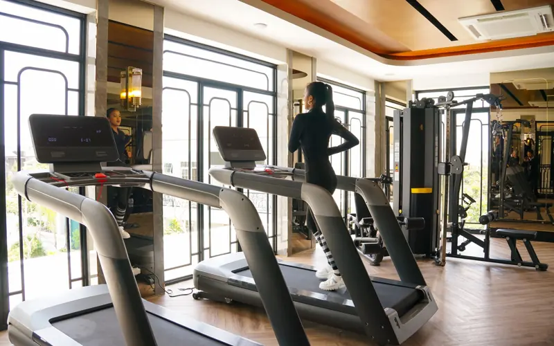 Young woman exercising on treadmill at a modern indoor gym with bright windows.