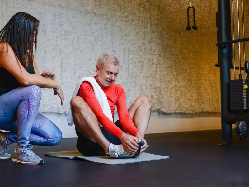 Senior man stretching on yoga mat with coach in gym for a healthy lifestyle.