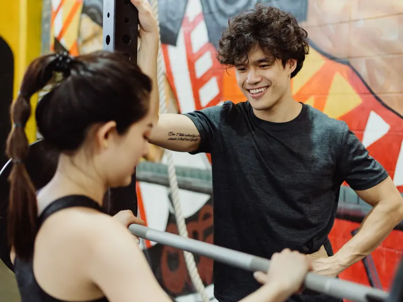 Smiling personal trainer coaching a woman lifting weights at the gym.