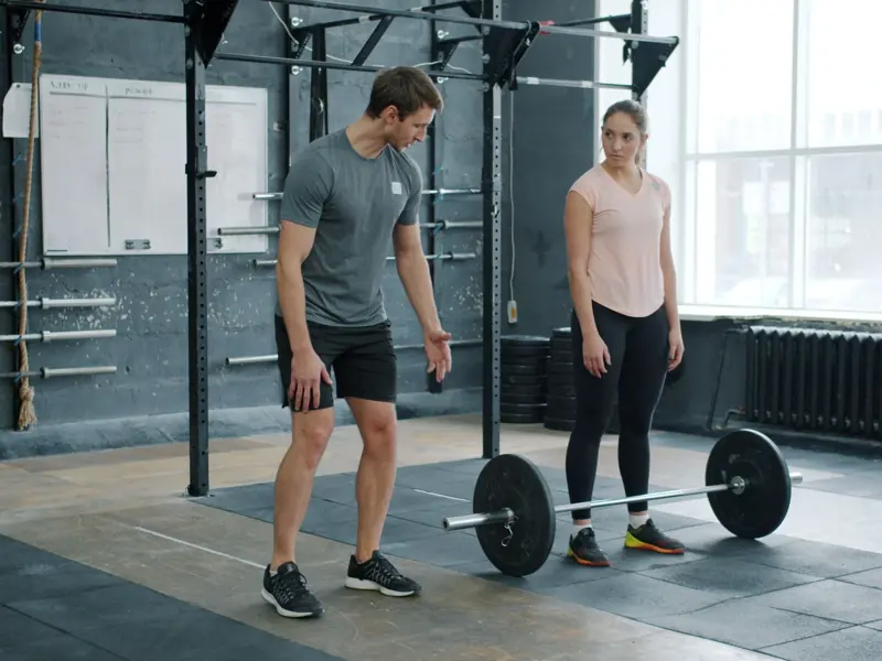 A personal trainer instructing a woman on barbell lifting technique in a gym setting.