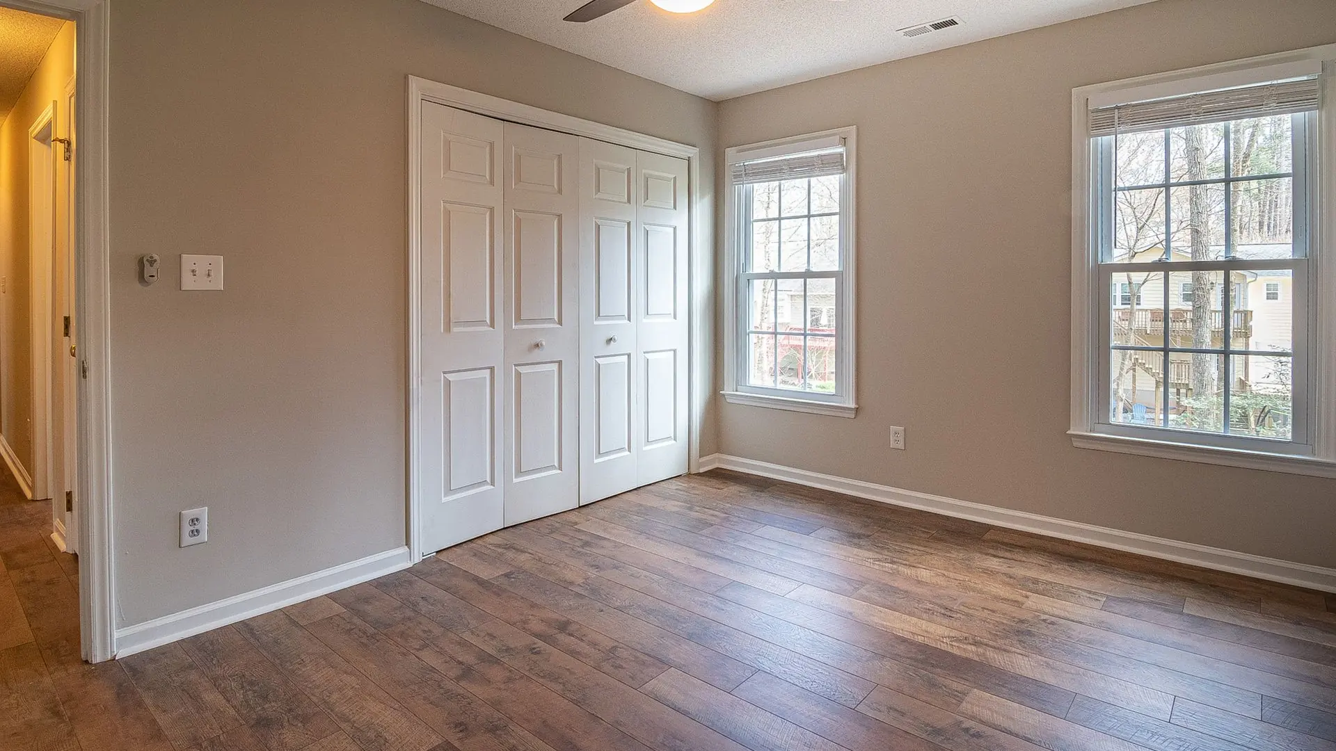 Spacious empty room with hardwood floors, ceiling fan, and natural light from windows.