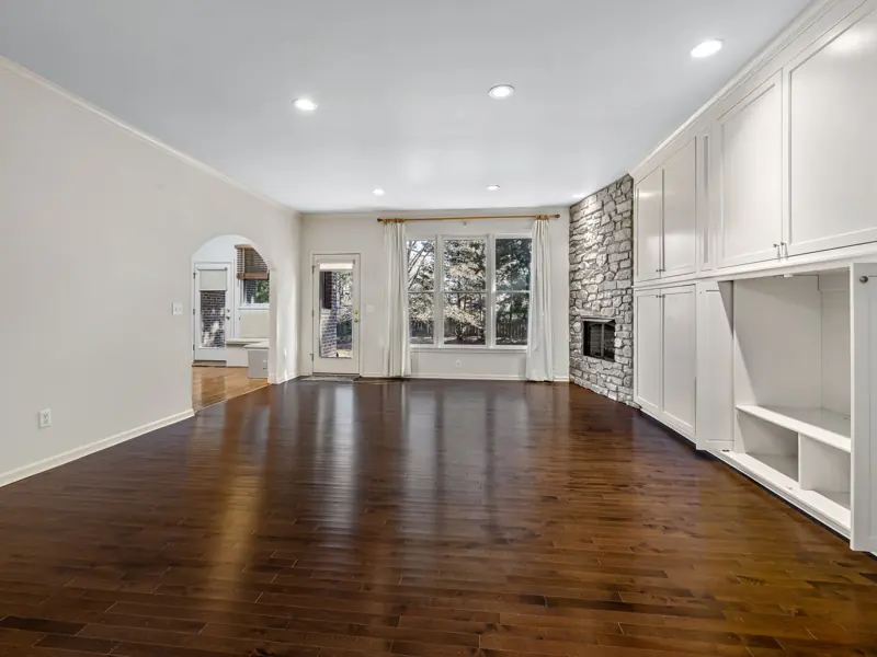 Bright, empty living room featuring hardwood floors and stone fireplace.