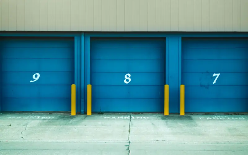 Three blue shutter doors numbered 9, 8, and 7 with yellow barriers in urban environment.