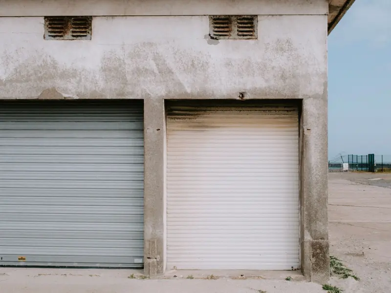 A detailed view of a weathered industrial building façade with rusty roll-up doors and a concrete exterior.