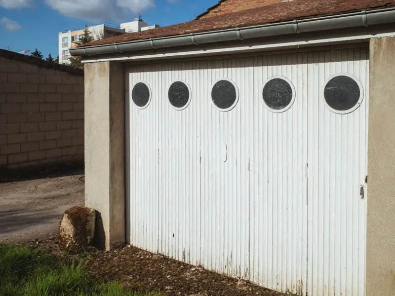 White garage door with circular windows in a residential area of Compiègne, France.