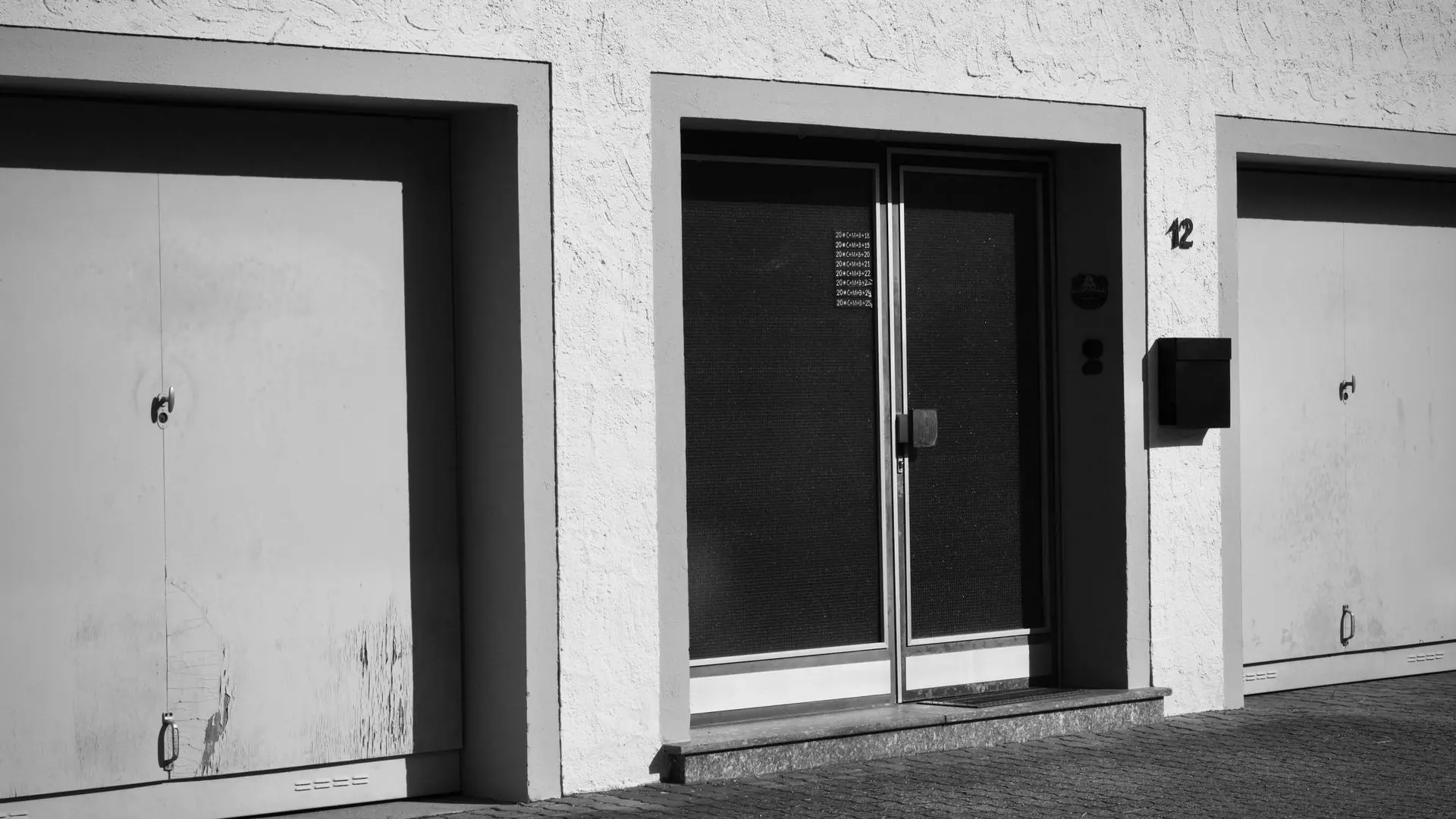 Monochrome photo of an urban building facade with garages and doors.