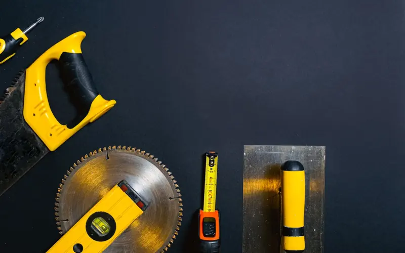 Hand tools arranged on a black surface, featuring saws, levels, and a tape measure.