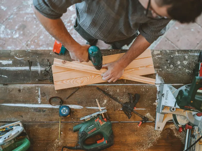 Craftsman busy drilling wooden planks in a carpentry workshop with various tools around.