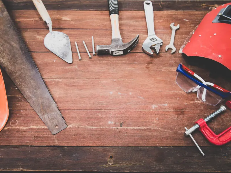 Flat lay of various workshop tools on a rustic wooden table, showcasing DIY essentials.