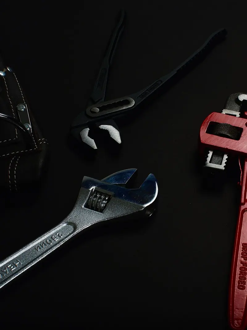 Close-up of various hand tools including wrenches and pliers on a dark surface.