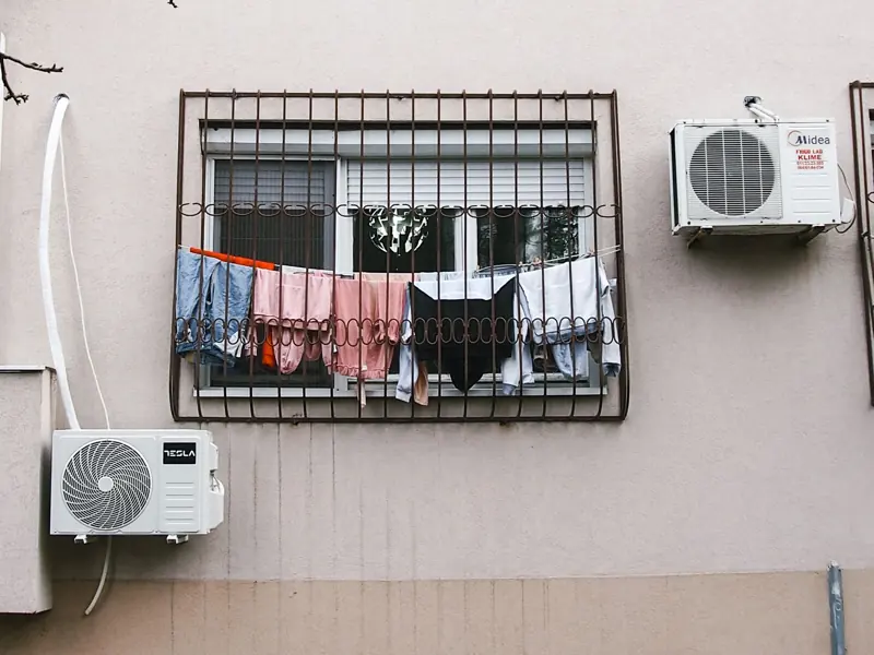 Clothes hanging to dry on a barred window with air conditioners in an urban setting.