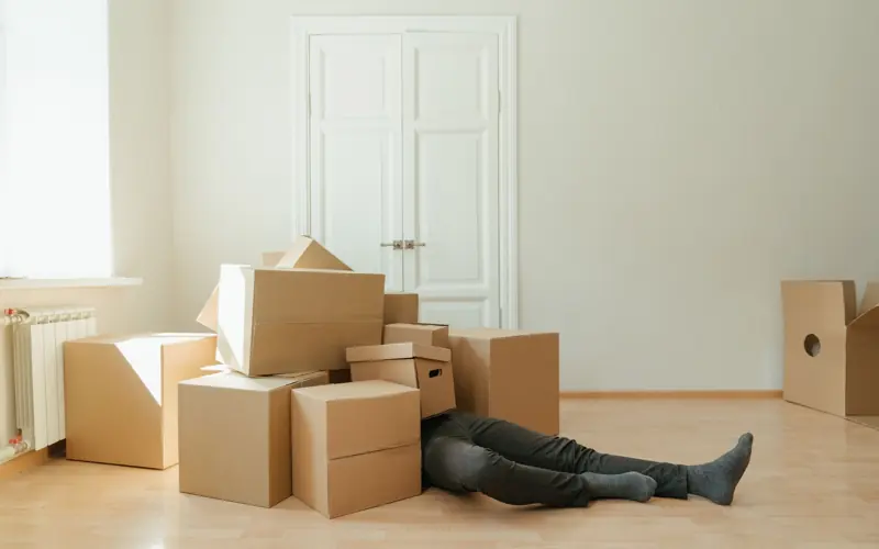 Person on floor surrounded by cardboard boxes during moving; concept of stress and relocation.