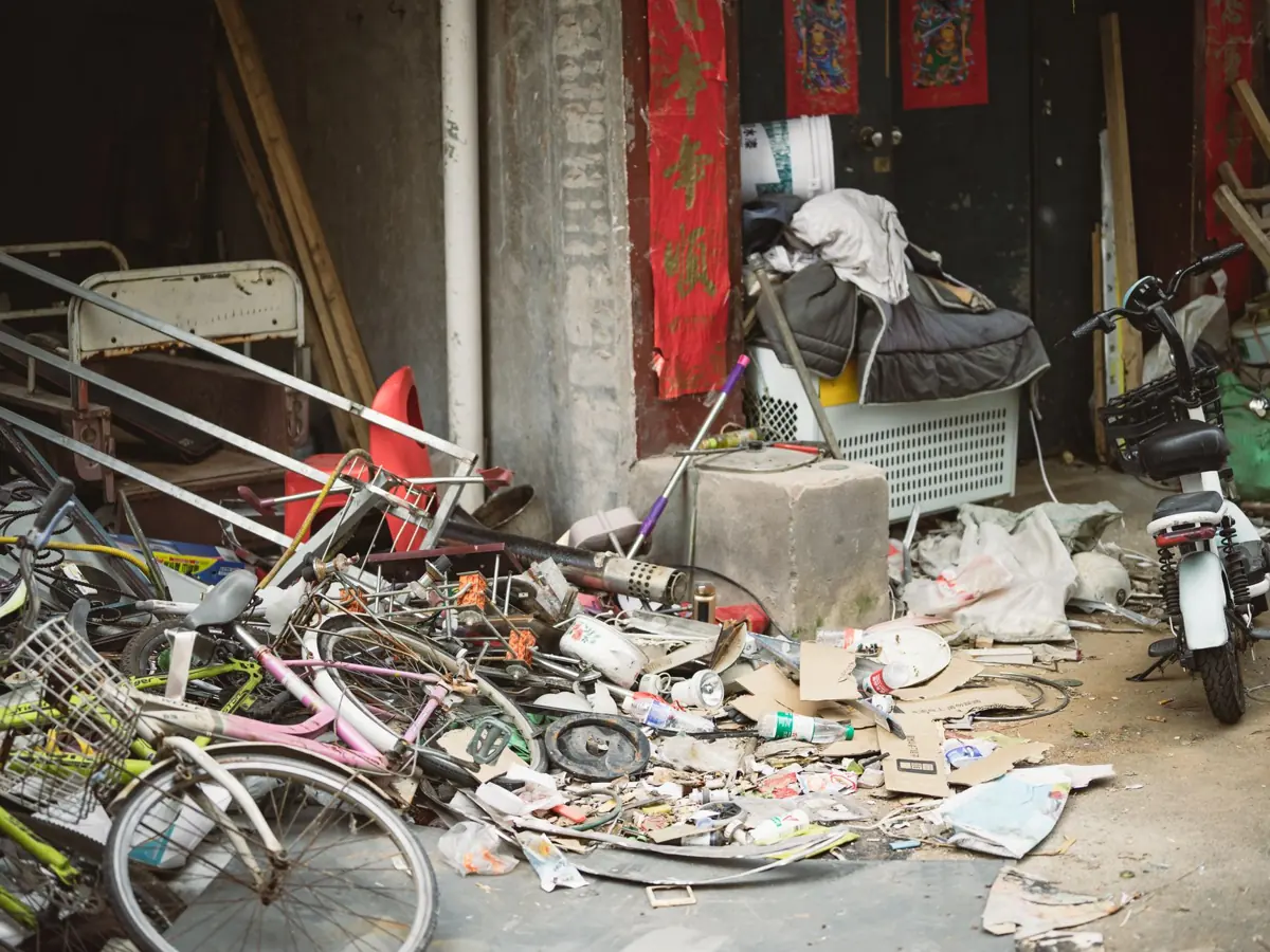 A cluttered alley filled with old bicycles, scrap metal, and miscellaneous debris beside a building.