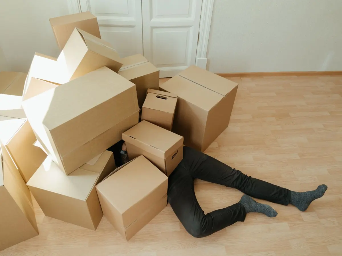 A person overwhelmed by cardboard boxes during a home move, symbolizing stress and relocation.