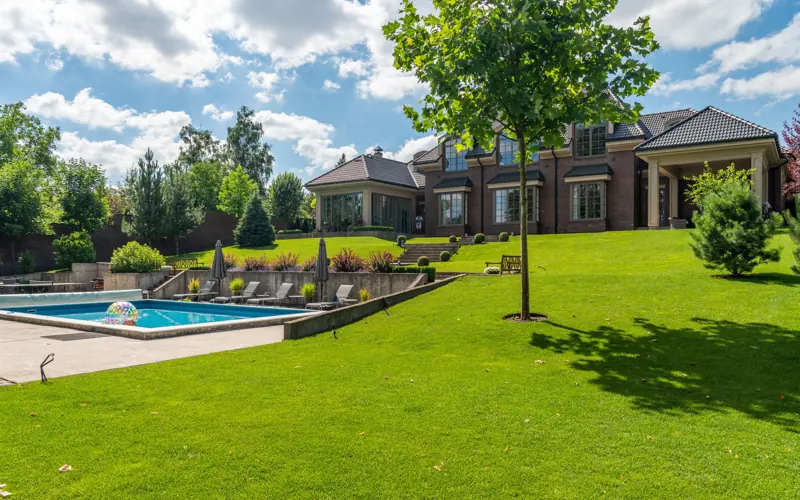 Spacious elegant mansion with a pristine pool, lush garden, and clear blue sky.
