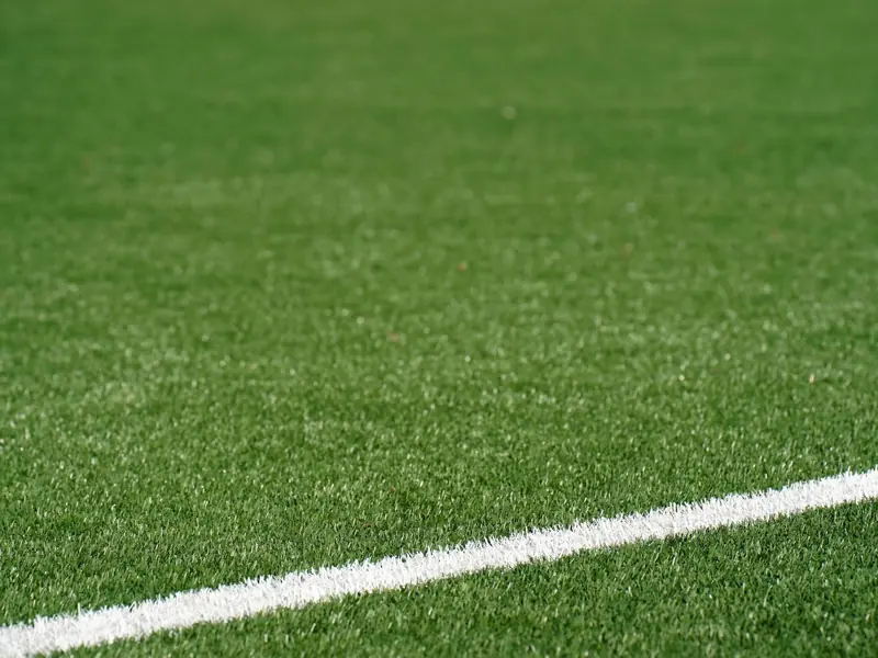 Close-up view of a green artificial soccer field with a white boundary line and space for text.