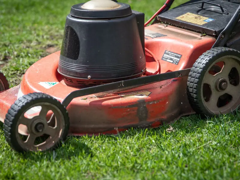 A close-up view of a red lawn mower on a green lawn, showcasing its details.
