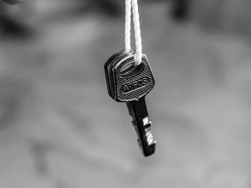 Monochrome image of a key hanging on a string, emphasizing security concepts.