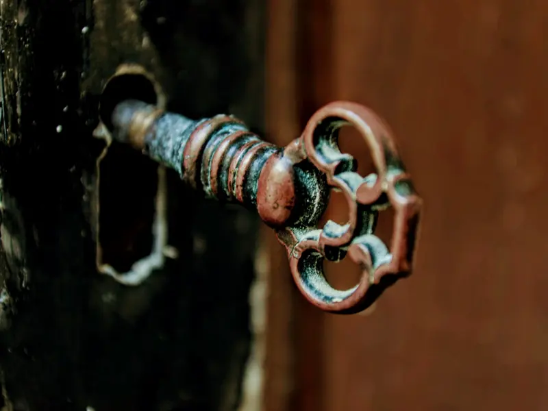 Close-up of an antique iron key fitted in an old wooden door's keyhole.
