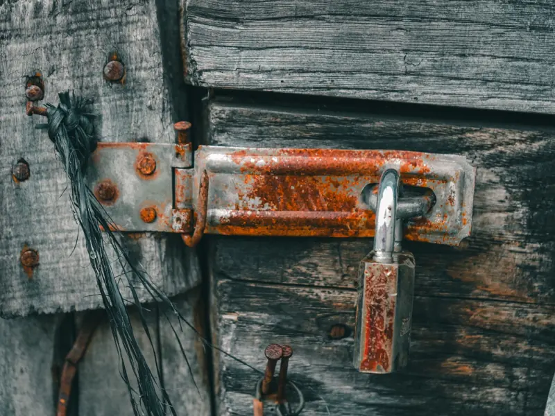 Close-up of a rusty padlock on an old wooden door, showing texture and decay.