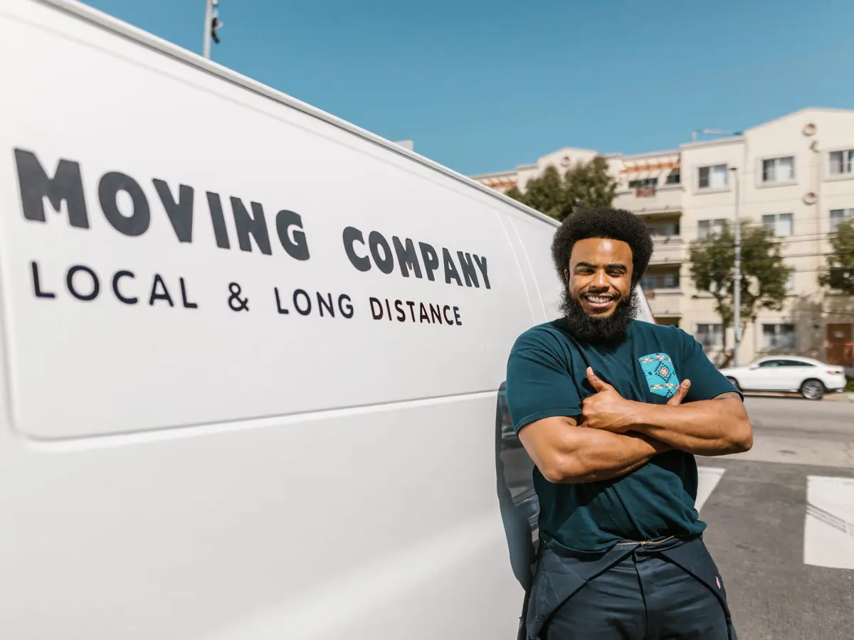 A cheerful mover standing confidently beside a moving company's van, ready for local or long distance relocation services.